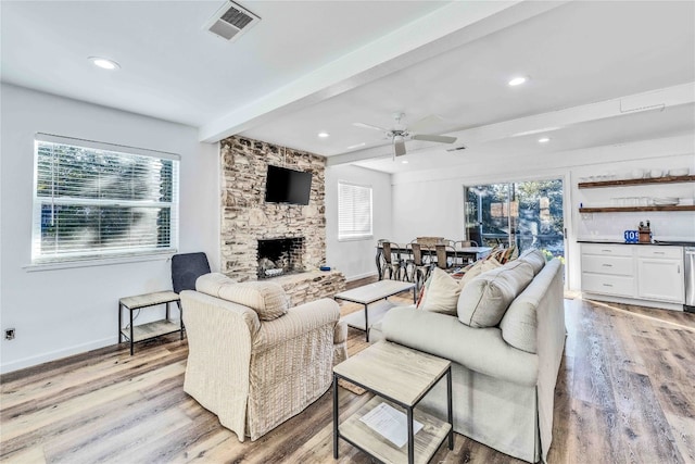 living room with beam ceiling, a fireplace, light wood-type flooring, and plenty of natural light