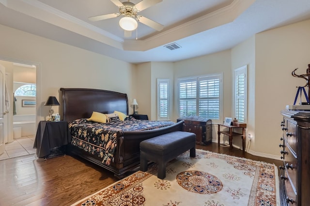 bedroom with a tray ceiling, connected bathroom, multiple windows, and light wood-type flooring