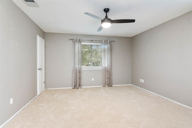 spare room with light colored carpet, baseboards, a ceiling fan, and visible vents