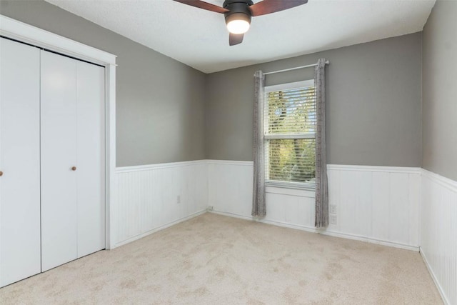 unfurnished bedroom with a closet, a wainscoted wall, carpet flooring, and ceiling fan