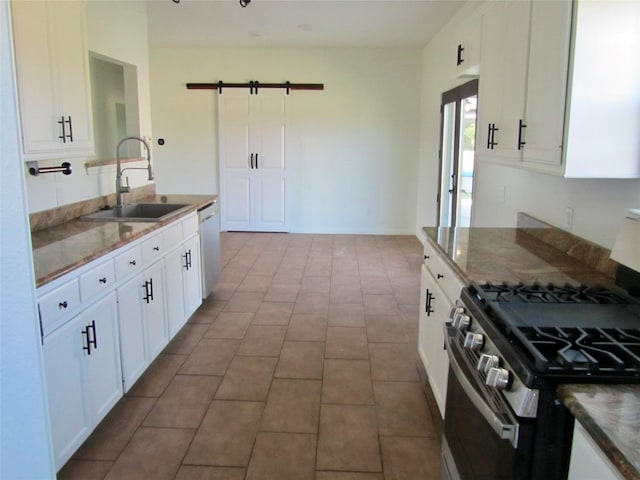 kitchen with stainless steel appliances, dark stone countertops, sink, a barn door, and white cabinetry