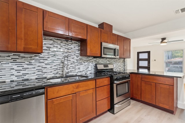 kitchen featuring appliances with stainless steel finishes, sink, kitchen peninsula, light hardwood / wood-style floors, and decorative backsplash