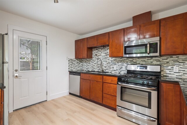 kitchen featuring appliances with stainless steel finishes, decorative backsplash, sink, and light wood-type flooring