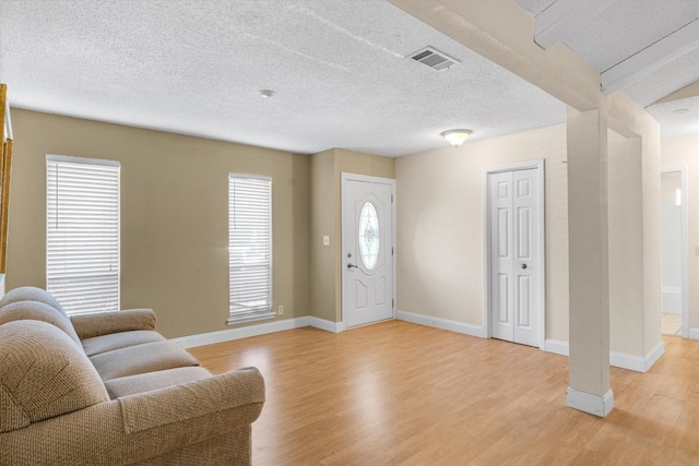 entrance foyer with a textured ceiling, a healthy amount of sunlight, light hardwood / wood-style flooring, and beam ceiling