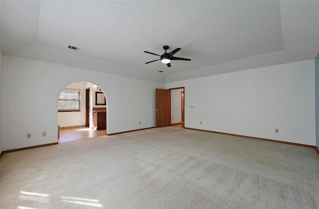 carpeted spare room with ceiling fan, a textured ceiling, and a tray ceiling