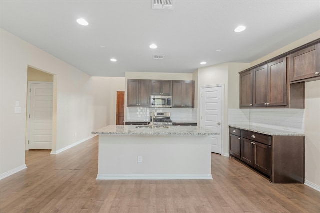 kitchen with light hardwood / wood-style floors, appliances with stainless steel finishes, light stone counters, and dark brown cabinets