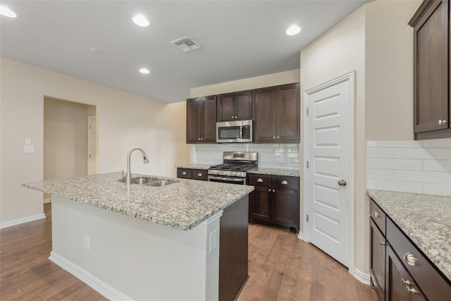 kitchen with appliances with stainless steel finishes, sink, dark brown cabinetry, light hardwood / wood-style flooring, and a kitchen island with sink