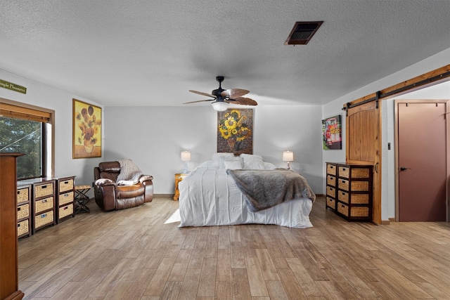 bedroom featuring a textured ceiling, a barn door, light hardwood / wood-style floors, and ceiling fan