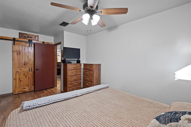 bedroom featuring light wood-type flooring, ceiling fan, and a barn door