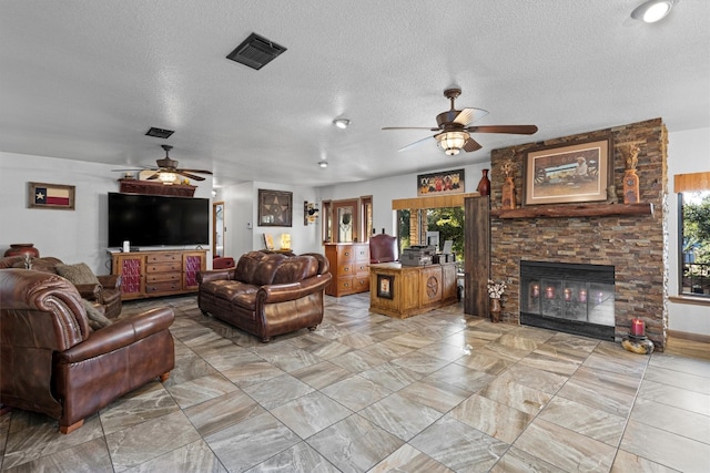 living room with ceiling fan, a stone fireplace, and a textured ceiling