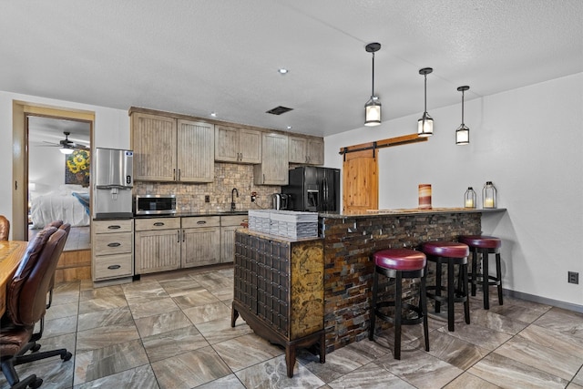 kitchen featuring a barn door, black fridge, decorative light fixtures, a breakfast bar area, and decorative backsplash