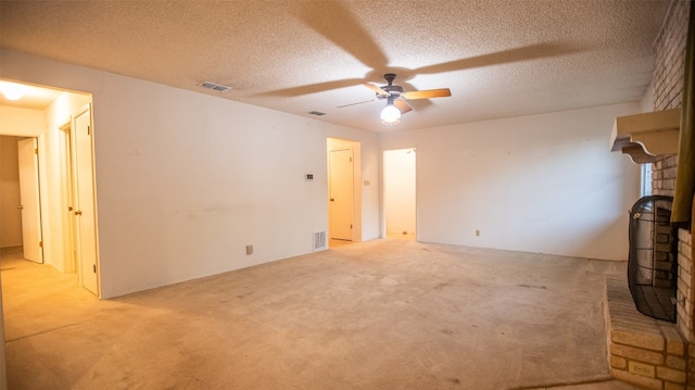 unfurnished living room featuring ceiling fan, a textured ceiling, a wood stove, and light colored carpet