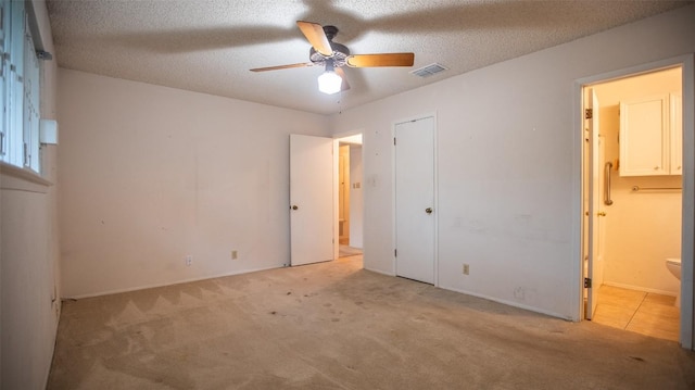 unfurnished bedroom with connected bathroom, a textured ceiling, visible vents, and light carpet