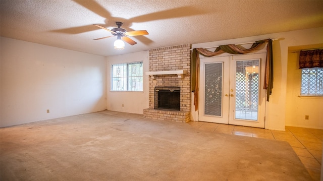 unfurnished living room featuring light tile patterned floors, ceiling fan, a textured ceiling, a fireplace, and french doors