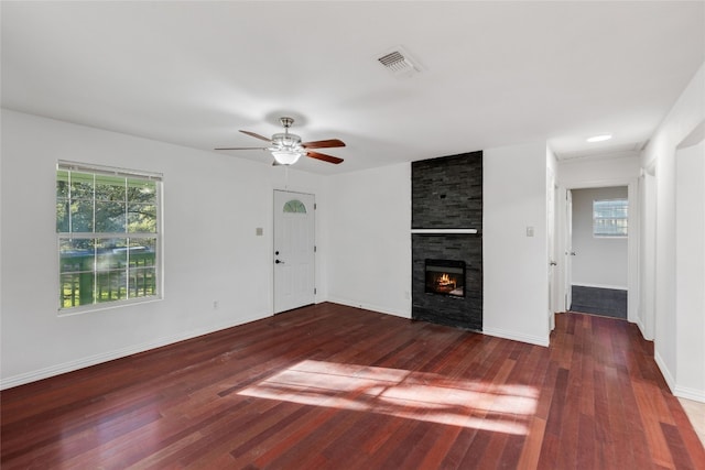 unfurnished living room featuring dark wood-type flooring, ceiling fan, and a stone fireplace