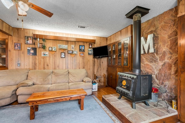 living room with wooden walls, a textured ceiling, hardwood / wood-style flooring, and a wood stove