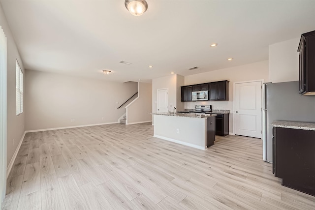 kitchen with light stone countertops, light hardwood / wood-style flooring, stainless steel appliances, and an island with sink