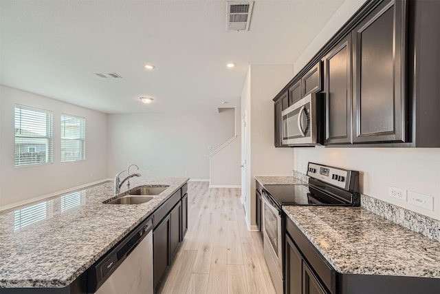 kitchen with light stone countertops, appliances with stainless steel finishes, sink, a kitchen island with sink, and light wood-type flooring