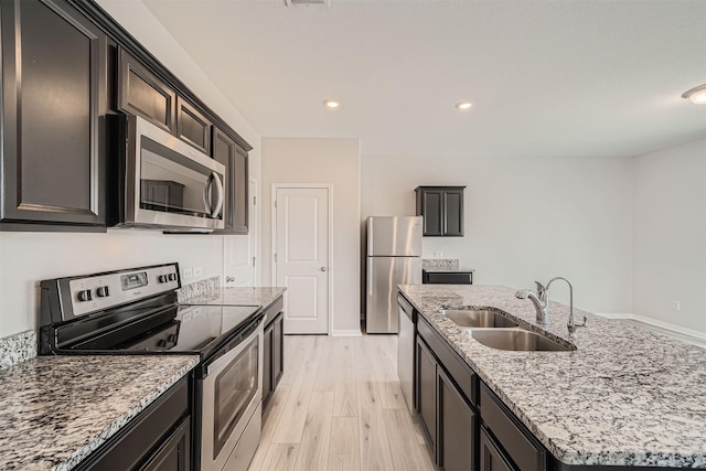 kitchen with light hardwood / wood-style floors, a center island with sink, sink, appliances with stainless steel finishes, and light stone counters