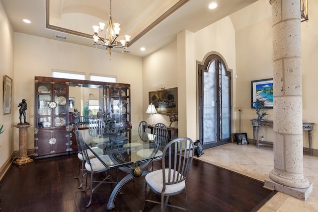 dining room featuring hardwood / wood-style floors, ornate columns, a chandelier, and a high ceiling