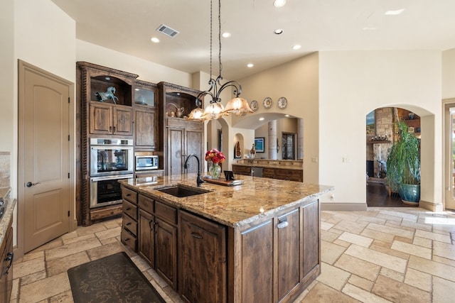 kitchen featuring dark brown cabinets, an island with sink, appliances with stainless steel finishes, pendant lighting, and sink