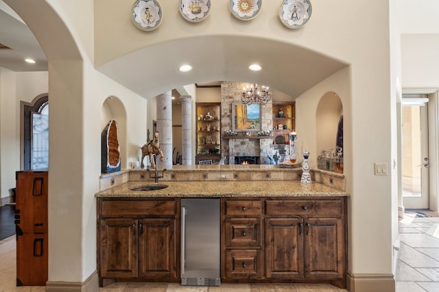 bar with a notable chandelier, light stone countertops, sink, and dark brown cabinets