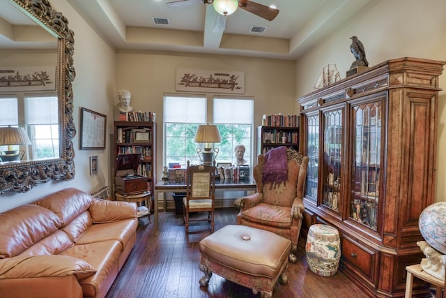 living room featuring dark wood-type flooring, a raised ceiling, and ceiling fan