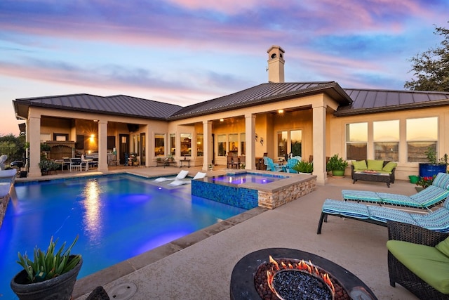 pool at dusk with an in ground hot tub, a patio area, and an outdoor living space with a fire pit