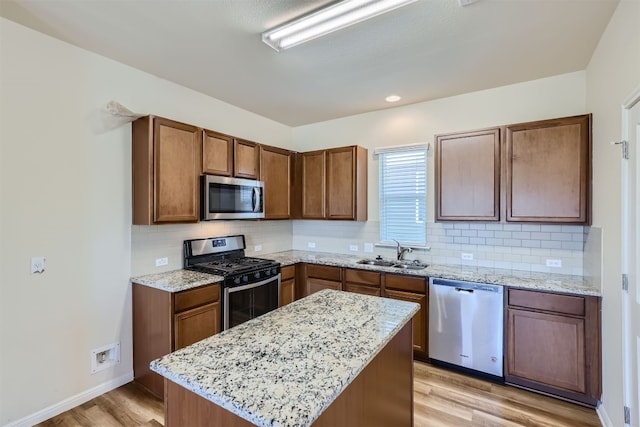 kitchen with stainless steel appliances, light stone countertops, sink, and light wood-type flooring