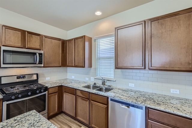 kitchen with decorative backsplash, light wood-type flooring, stainless steel appliances, sink, and light stone counters