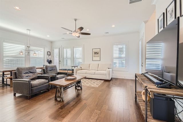 living room with crown molding, ceiling fan with notable chandelier, hardwood / wood-style flooring, and a healthy amount of sunlight