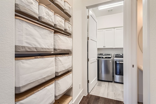 clothes washing area featuring washer and dryer, cabinets, and light hardwood / wood-style flooring