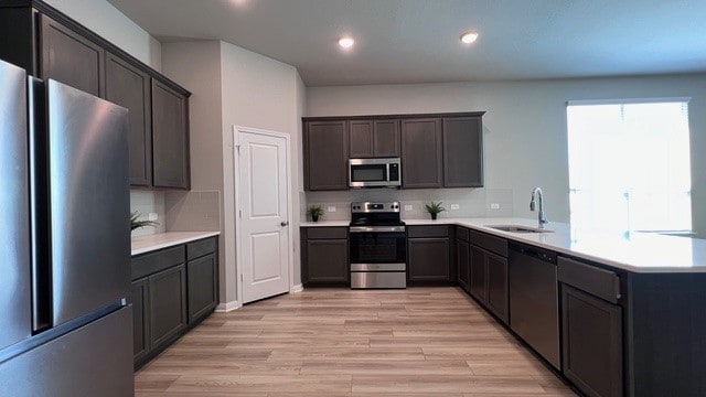 kitchen with appliances with stainless steel finishes, sink, dark brown cabinets, kitchen peninsula, and light hardwood / wood-style flooring