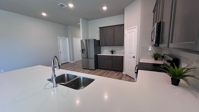 kitchen with decorative backsplash, dark brown cabinets, sink, light hardwood / wood-style floors, and stainless steel appliances