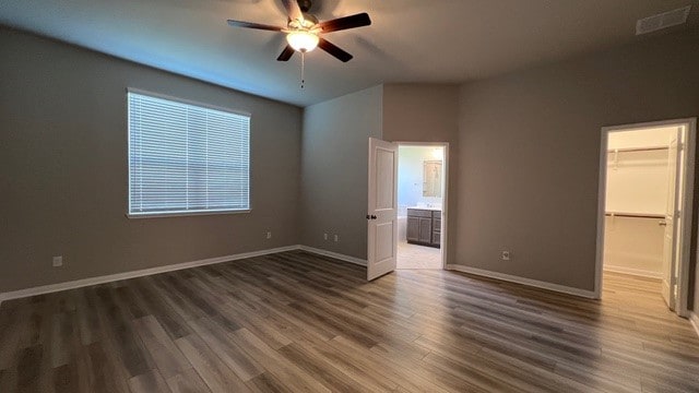 unfurnished bedroom featuring a closet, a walk in closet, ceiling fan, and dark hardwood / wood-style flooring