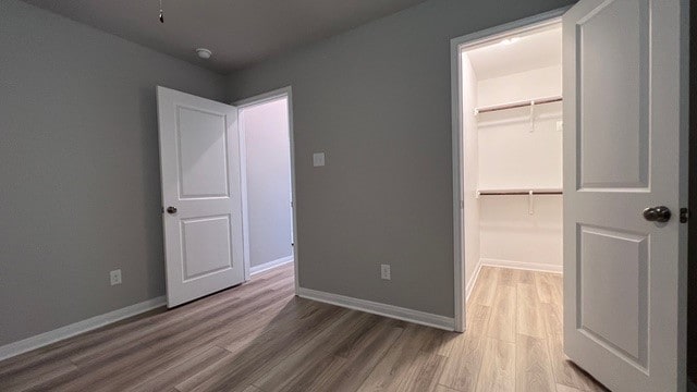 unfurnished bedroom featuring wood-type flooring, a walk in closet, and a closet