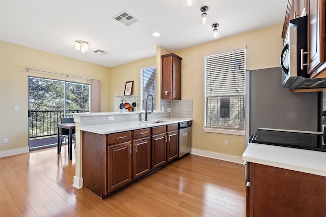 kitchen featuring kitchen peninsula, backsplash, sink, appliances with stainless steel finishes, and light hardwood / wood-style floors