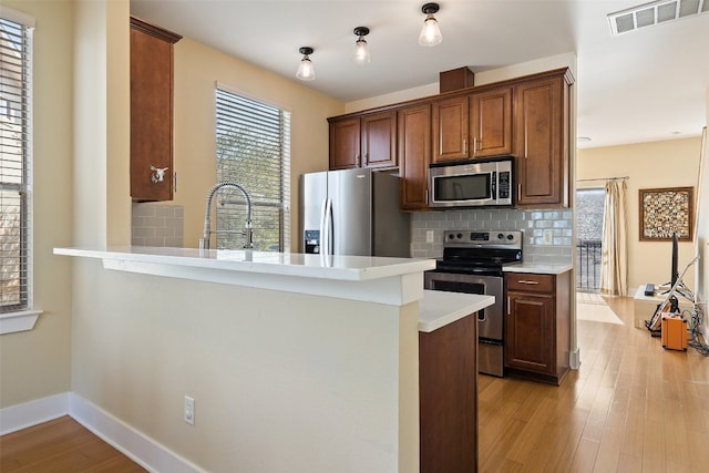 kitchen featuring tasteful backsplash, appliances with stainless steel finishes, sink, light wood-type flooring, and kitchen peninsula