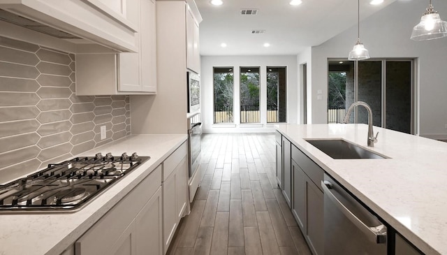 kitchen featuring stainless steel appliances, a sink, visible vents, wall chimney range hood, and dark wood-style floors