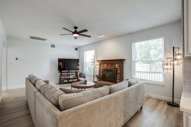 living room featuring ceiling fan, a brick fireplace, light wood-type flooring, and plenty of natural light