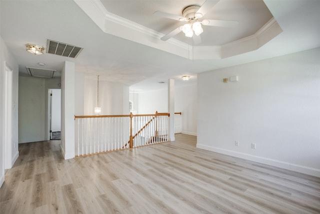 empty room with light hardwood / wood-style flooring, ceiling fan, a raised ceiling, and crown molding