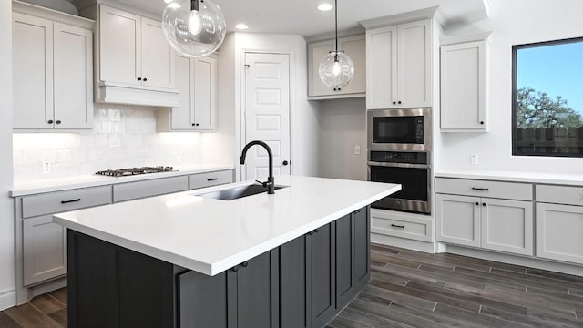 kitchen featuring stainless steel appliances, decorative light fixtures, sink, and a center island with sink