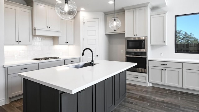 120 Teakmill Trl, San Marcos, TX 78666 - kitchen with appliances with stainless steel finishes, a sink, dark wood-style floors, decorative backsplash, and a center island with sink