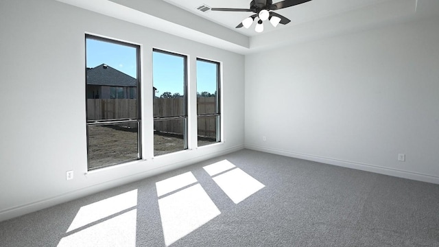 carpeted spare room with a raised ceiling and ceiling fan