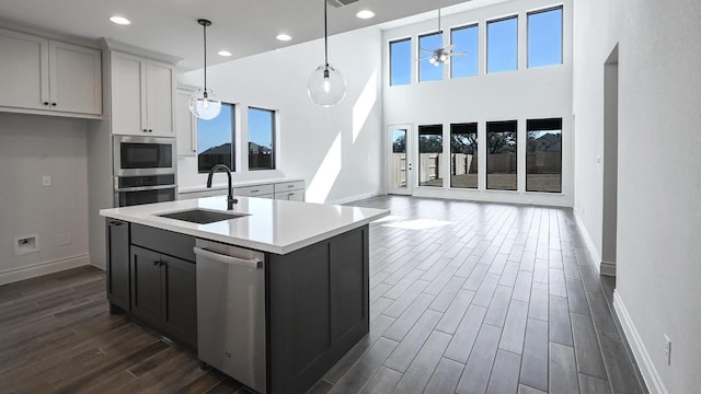 kitchen featuring appliances with stainless steel finishes, a wealth of natural light, pendant lighting, sink, and a center island with sink