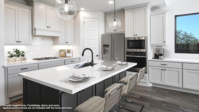 kitchen featuring sink, decorative light fixtures, stainless steel appliances, a kitchen island with sink, and decorative backsplash