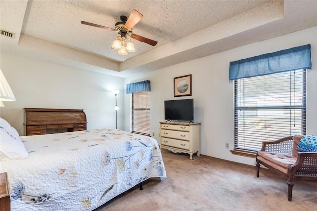 bedroom featuring visible vents, light colored carpet, a textured ceiling, and a tray ceiling