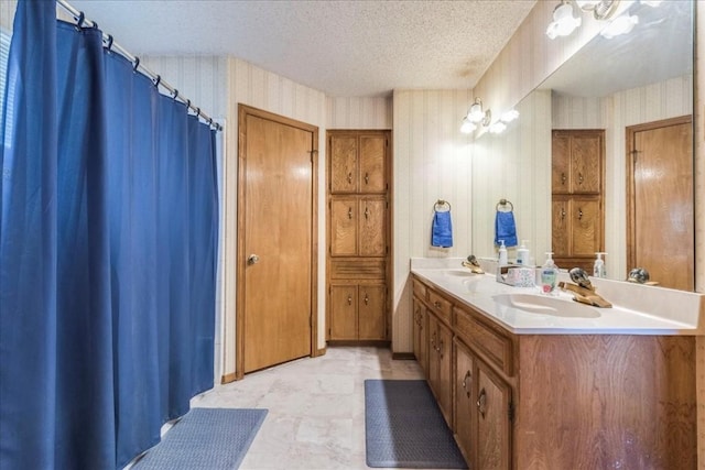 full bath with wallpapered walls, double vanity, a sink, and a textured ceiling