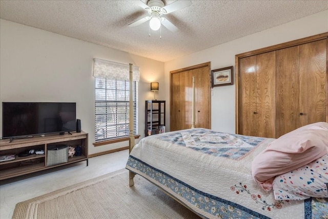 carpeted bedroom featuring ceiling fan, baseboards, two closets, and a textured ceiling