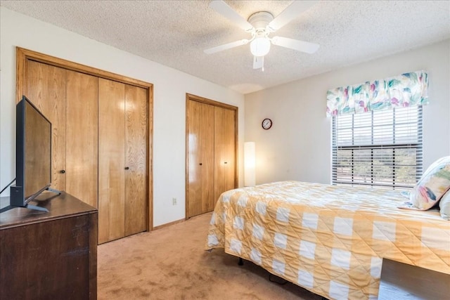 bedroom with a ceiling fan, light carpet, a textured ceiling, and multiple closets